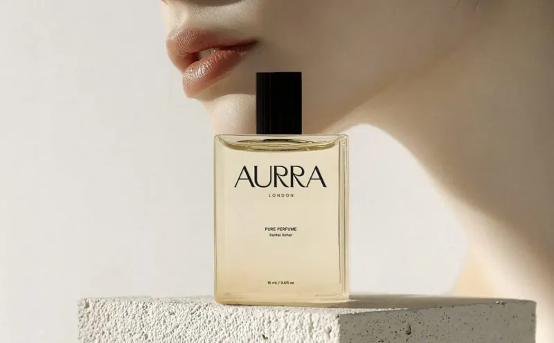 AURRA eau de parfum bottle on white stone, beside a woman's subtle profile, luxury perfume launch.