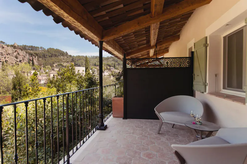 Spacious balcony with curved white chairs, wine glass on table, overlooking lush hills and Provençal village.