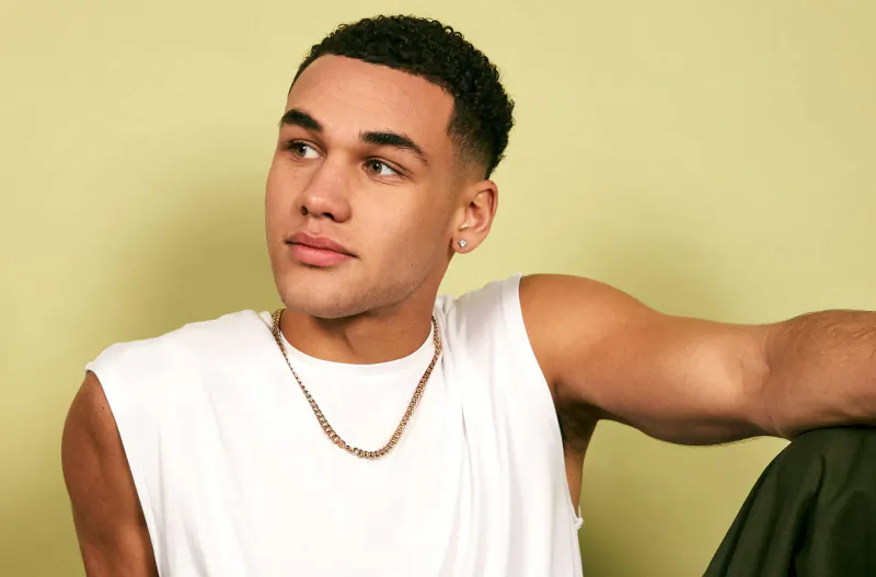 Young Black man with short hair, gold chain, and white tank top, posing against lime green background