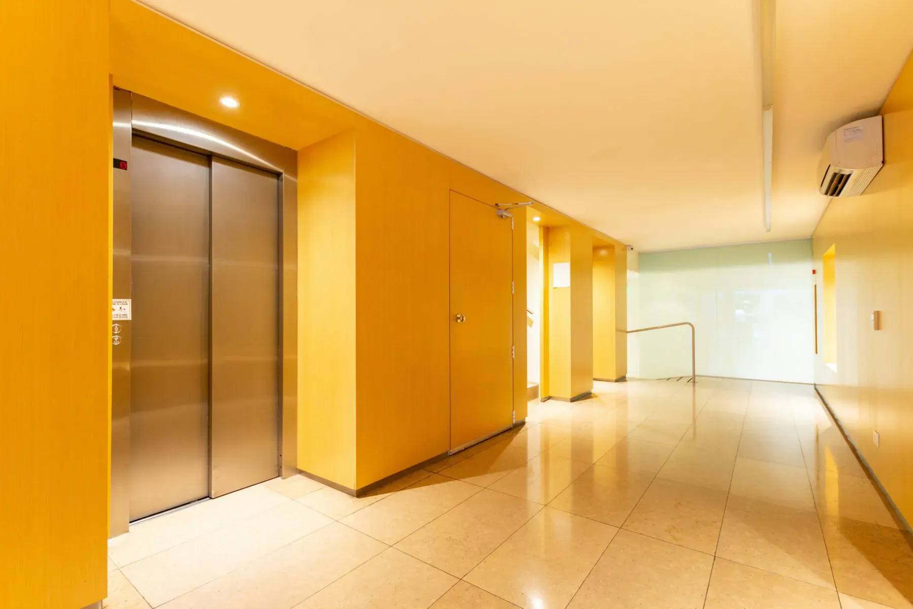 Modern yellow elevator doors in a brightly lit hallway with glossy tile floor