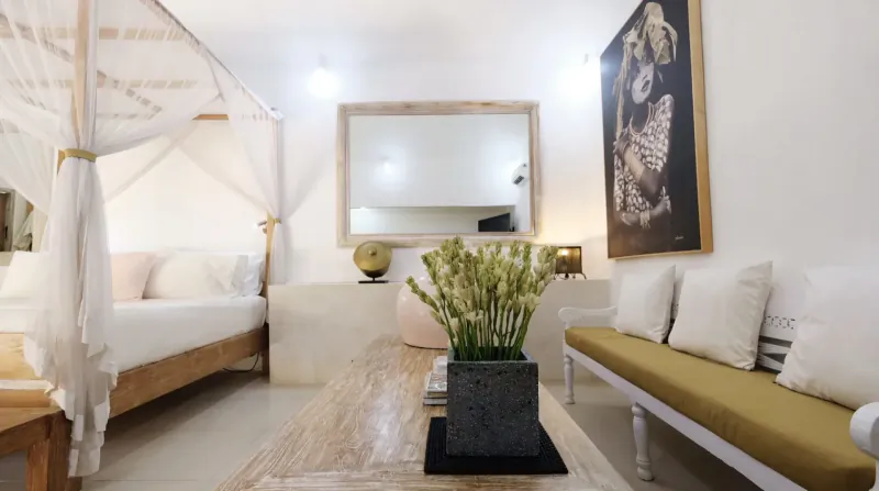 Luxurious Bali bedroom with white canopy bed, yellow sofa, flowers, art, and mirror.