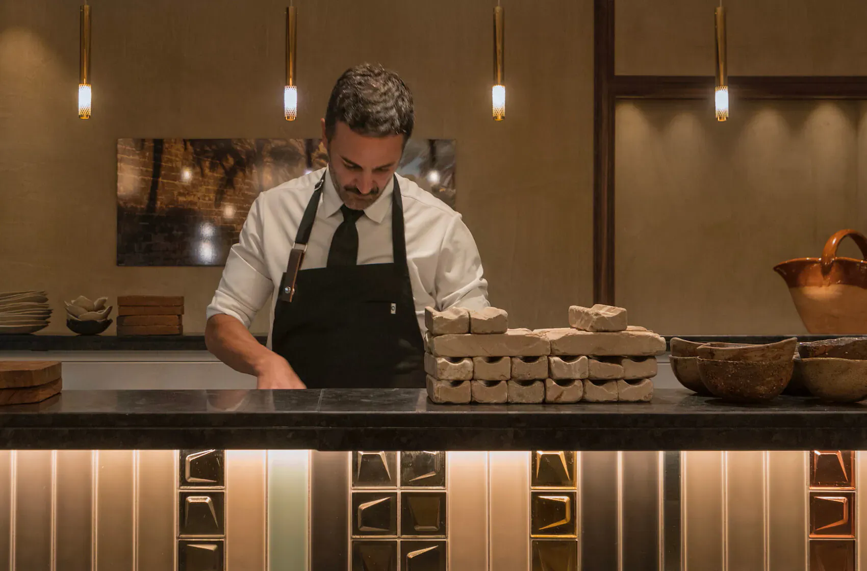 Chef in white shirt and black apron preparing tofu stacks on counter in modern El Llorenç kitchen