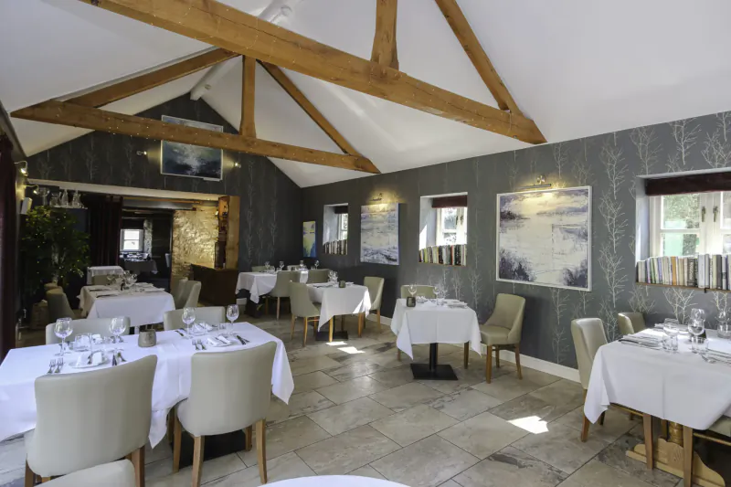 Elegant dining room at Nut Tree Inn with wooden beams, white tablecloths, set tables, and abstract wall art.