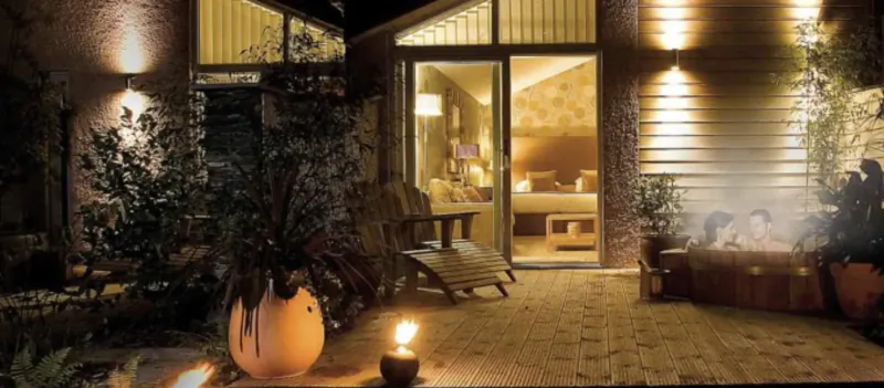 Twilight view of Gilpin Hotel's outdoor patio with lit plants, lantern, recliner, and open bedroom door.