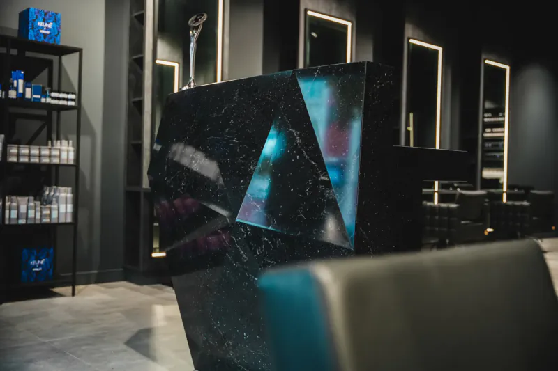 Modern black barber salon interior with black marble reception, blue product shelves, mirrors, and chairs.