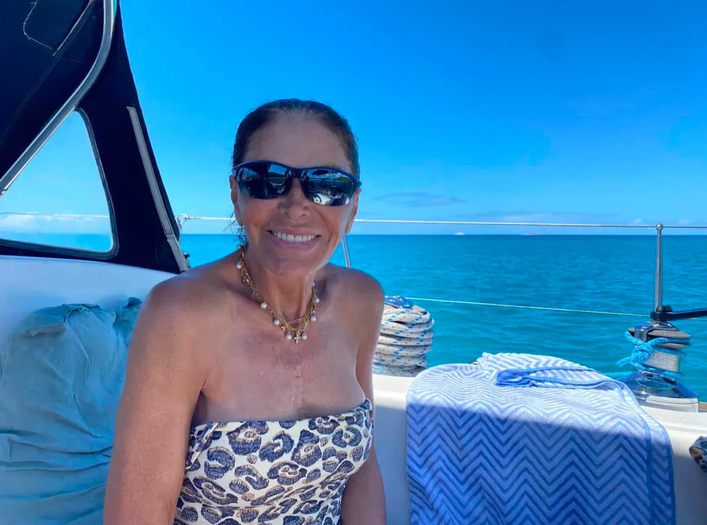 Mouna Ayoub smiles on luxury yacht in leopard print dress and sunglasses, turquoise sea backdrop