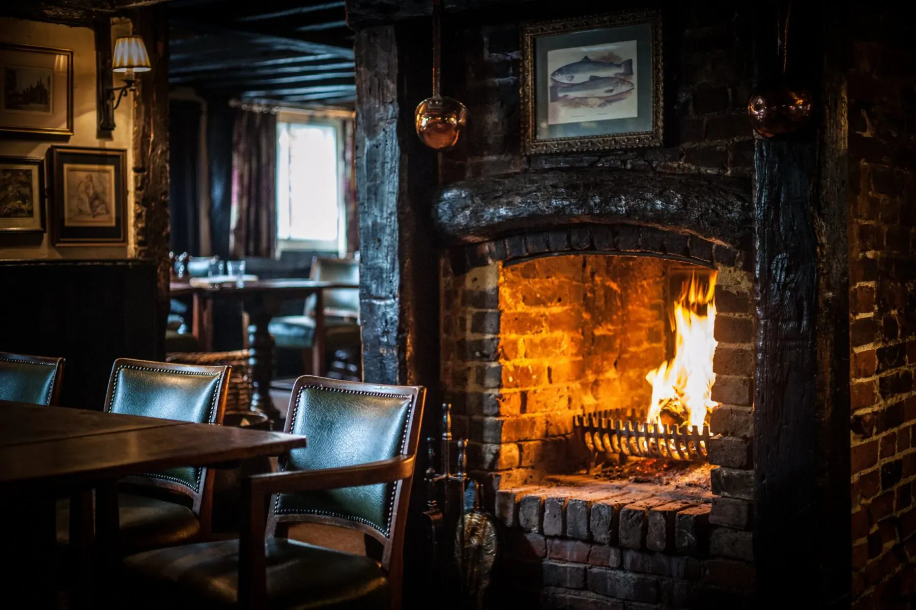 Cozy British pub interior with blazing stone fireplace, wooden tables, leather chairs, and nautical artwork.