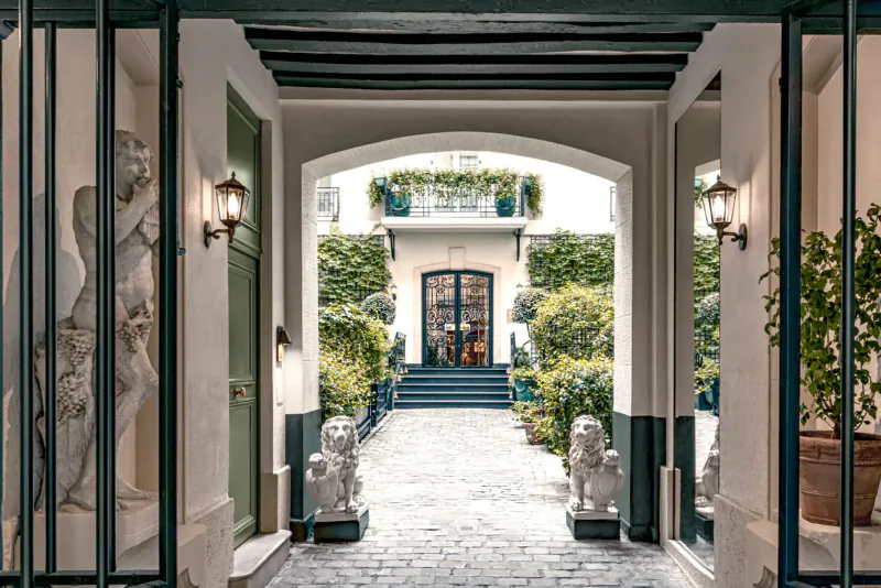 Elegant arched entrance gallery at Relais Christine Paris, with statues, lion guardians, plants, and steps to doors.