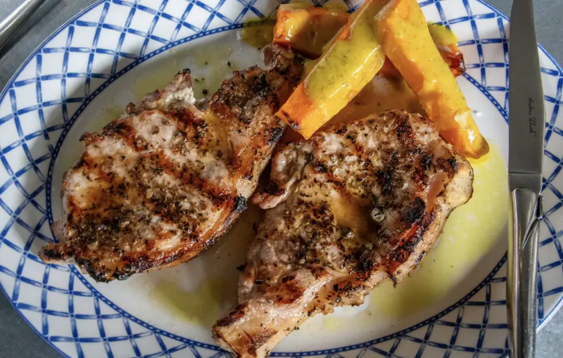 Two grilled pork chops with sweet potato fries on a blue-edged plate