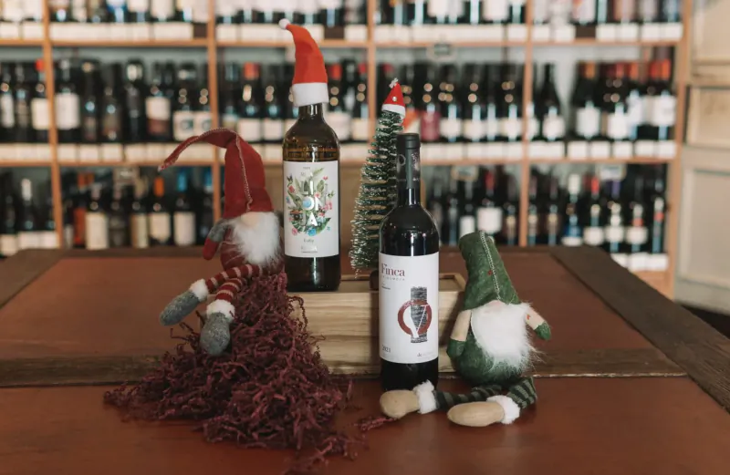 Christmas gnomes and wine bottles labeled Vivat Bacchus on table in wine shop with shelves behind