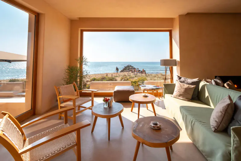 Cozy modern living room with wooden chairs, green sofa, coffee tables, overlooking sunny beach and sea at Gastro Beach in Palma.
