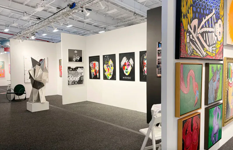 ArtExpo Dallas gallery booth with abstract sculptures, colorful paintings, white walls, and spotlights.