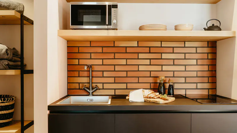 Modern kitchen in Candia Park Village with brick backsplash, black countertop, sink, microwave, and utensils.
