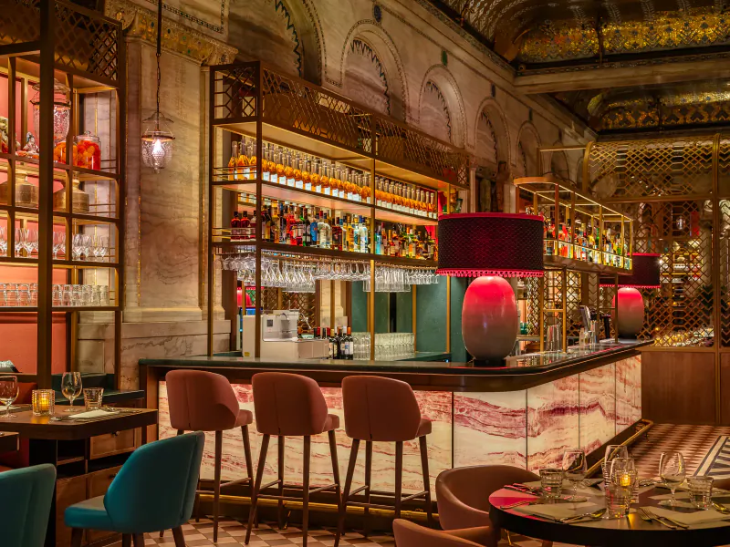 Opulent Masala Zone Piccadilly Circus brasserie bar with ornate architecture, lit shelves of liquor bottles, pink stools, and lamps.