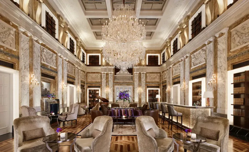 Opulent Hotel Imperial Vienna lobby with grand chandelier, ornate walls, plush seating, bar, and piano.
