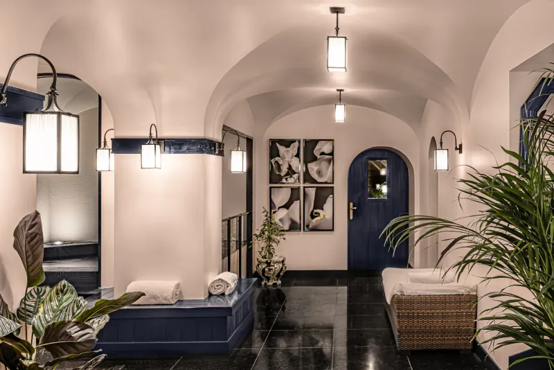 Elegant arched hotel lounge at Relais Christine with white orchids, plants, blue benches, towels, and wall lamps.