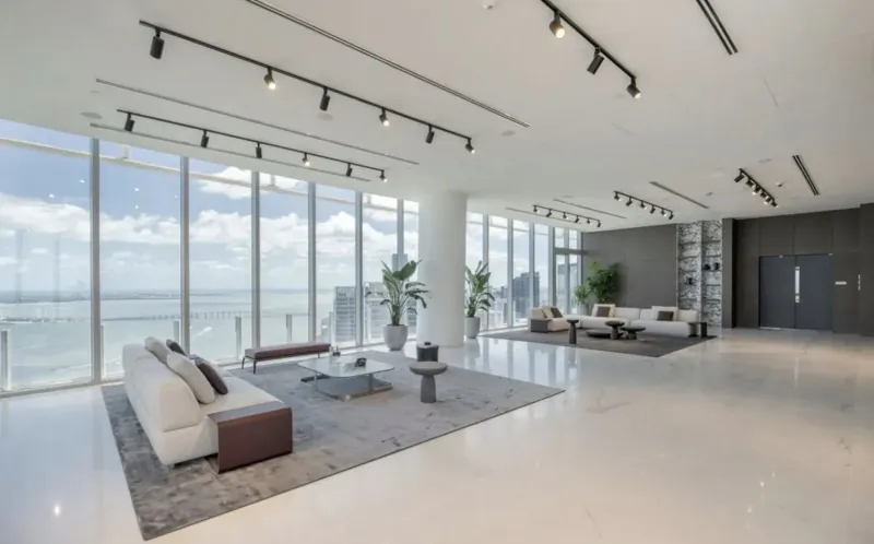 Spacious luxury lounge in Aston Martin Residences Miami with white sofas, plants, and ocean views through floor-to-ceiling windows.
