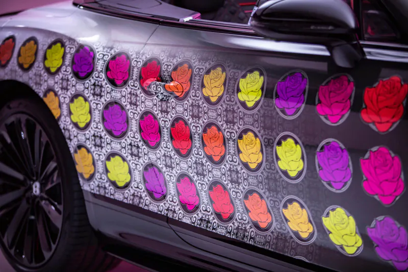 Close-up of Bentley's black car side with vibrant multicolored rose floral wrap design.