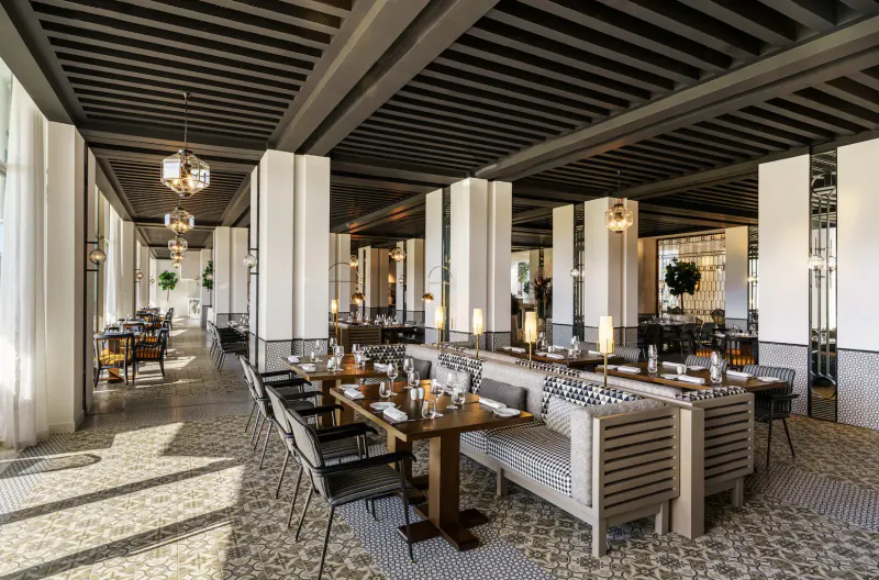 Elegant indoor dining area at Fairmont La Marina Rabat-Salé with wooden beamed ceiling, white columns, set tables, and plants.