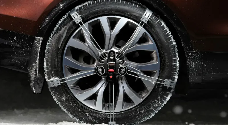 Close-up of stylish silver alloy wheel with snow chains on maroon Land Rover Discovery in snowy setting