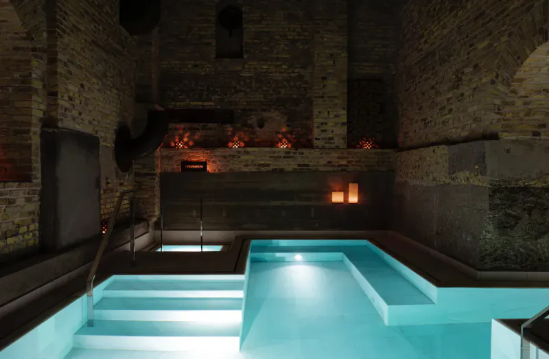 Candle-lit L-shaped turquoise pool in luxurious ancient brick bathhouse at Aire Ancient Baths London