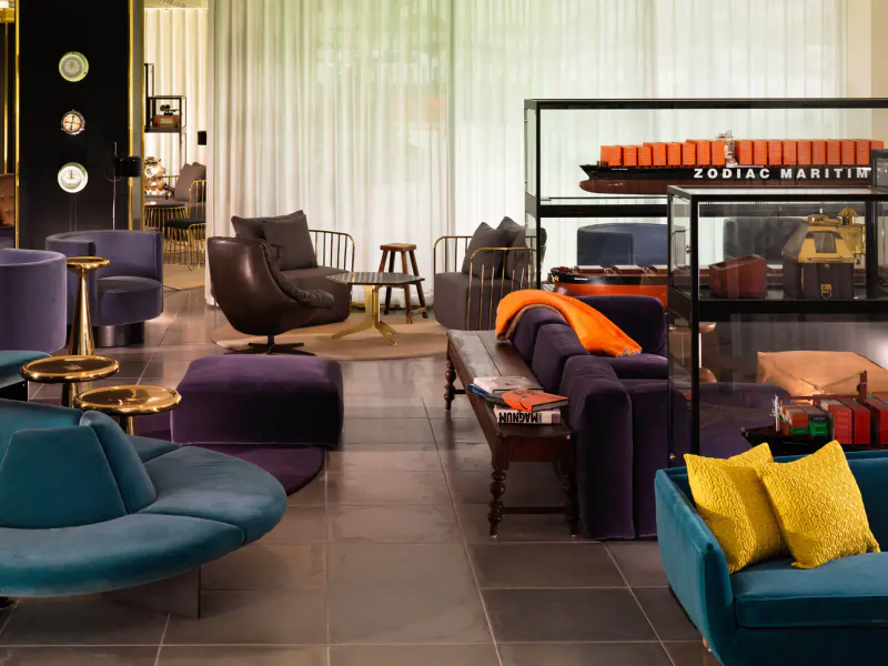 Elegant Sea Containers London hotel lounge with plush purple, teal, orange seating, model trains in glass case, sheer curtains.