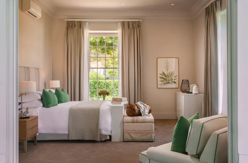 Elegant bedroom at Brookdale Wine Estate with green pillows on bed, window garden view, neutral tones.