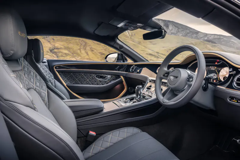 Bentley GT Mulliner Blackline interior: quilted black leather seats, wood trim, steering wheel, mountain view outside.