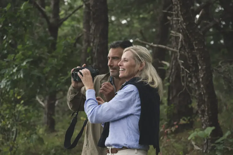Smiling couple in forest: man photographing with smart binoculars, woman beside him