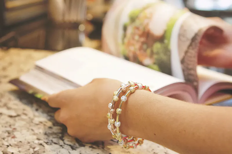 Woman's hand wearing multi-strand pearl bracelet, holding open book on kitchen counter near cookbook.