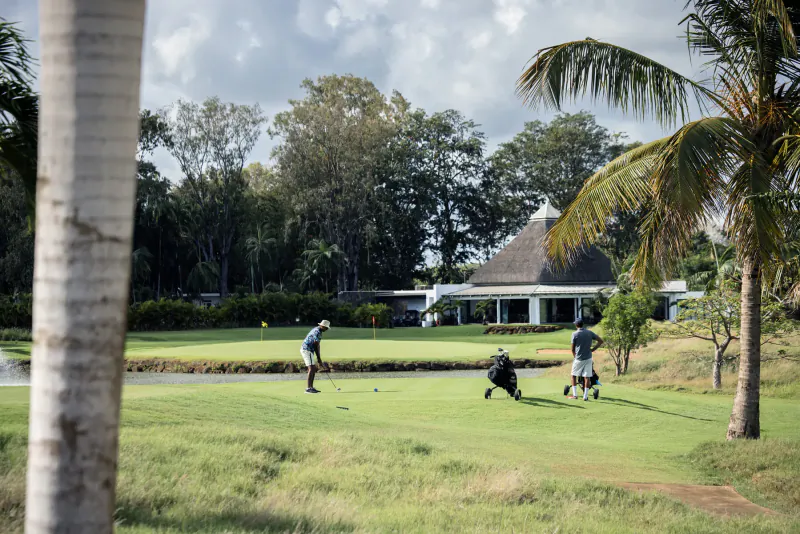 Golfers playing on lush green course near thatched-roof clubhouse and palm trees in Mauritius