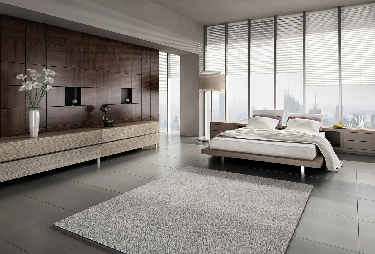 Modern luxury bedroom with platform bed, white lilies in vase, wood panel wall, and city skyline view through large windows.