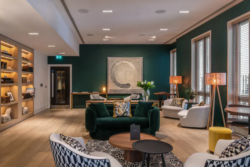 Elegant hotel lounge with green walls, plush green and white armchairs, round coffee tables, large abstract artwork, and plants