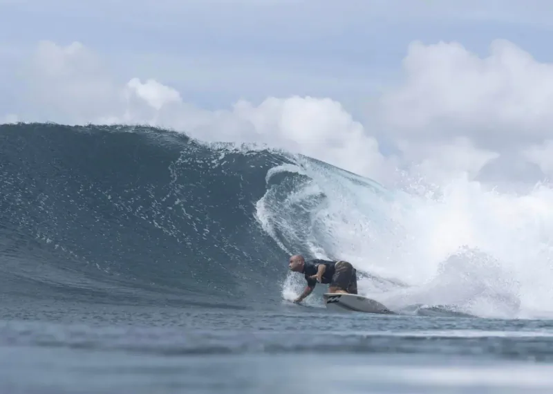 Surfer riding a massive curling wave in the Maldives, leaning into the barrel with whitewater spray.