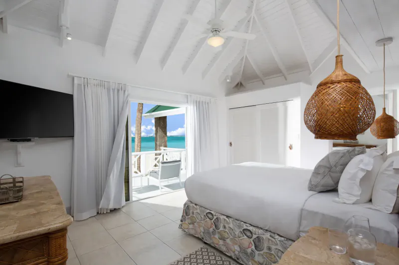 Spacious white bedroom at Palm Island Resort with king bed, rattan lamps, open doors to beach view.