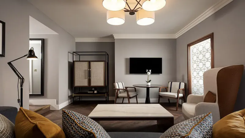 Elegant Parkgate Hotel Cardiff lounge with gray walls, modern chandelier, low coffee table, armchairs, TV, and vase.