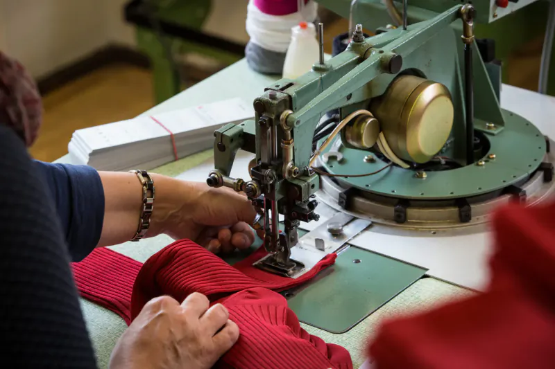 Worker sewing red fabric on vintage green industrial sewing machine at workstation
