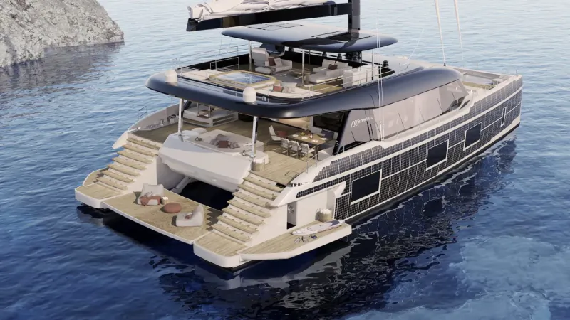 Sunreef 100 ECO luxury catamaran at stern view on water near rocky cliff, with decks, furniture, and sails.