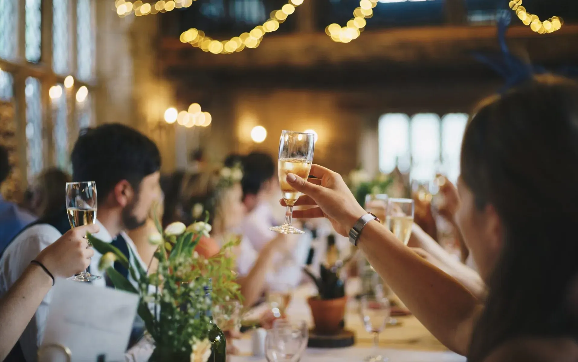 Group at elegant rustic venue toasting with champagne glasses amid flowers and warm lights