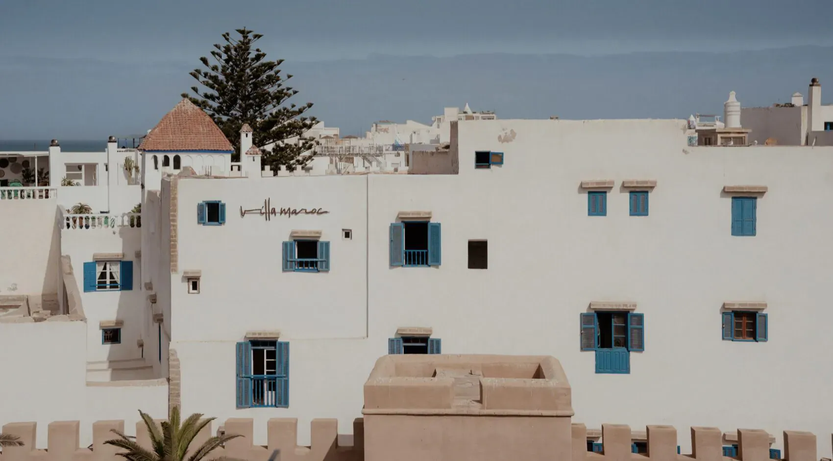 Whitewashed buildings with blue shutters and red-tiled roofs in Essaouira, Morocco, under clear sky