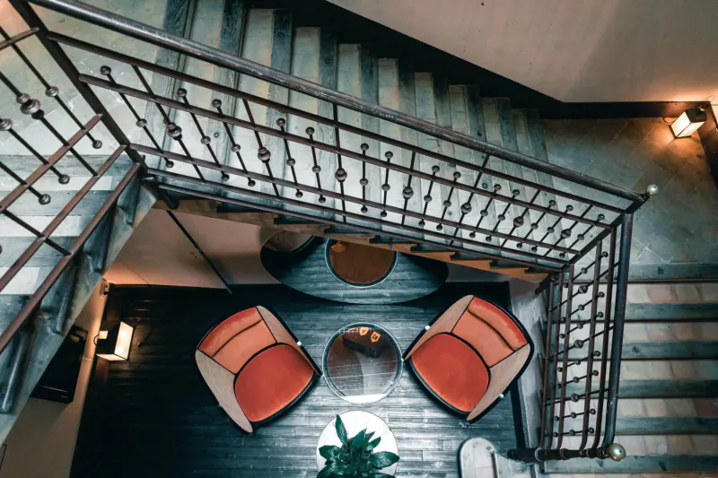 Overhead view of elegant spiral staircase with black metal railings surrounding orange chairs, round table, plant in luxury hotel lobby.