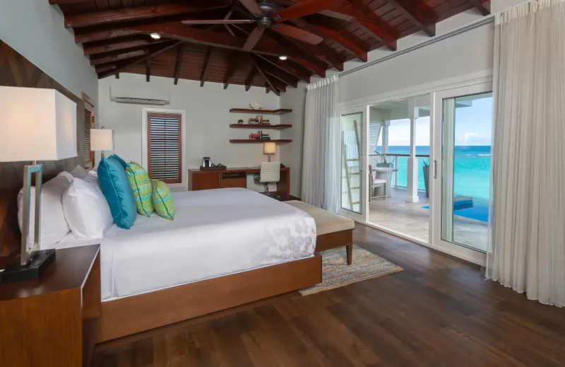 Luxurious bedroom at Hammock Cove Antigua with king bed, balcony, and turquoise ocean view.