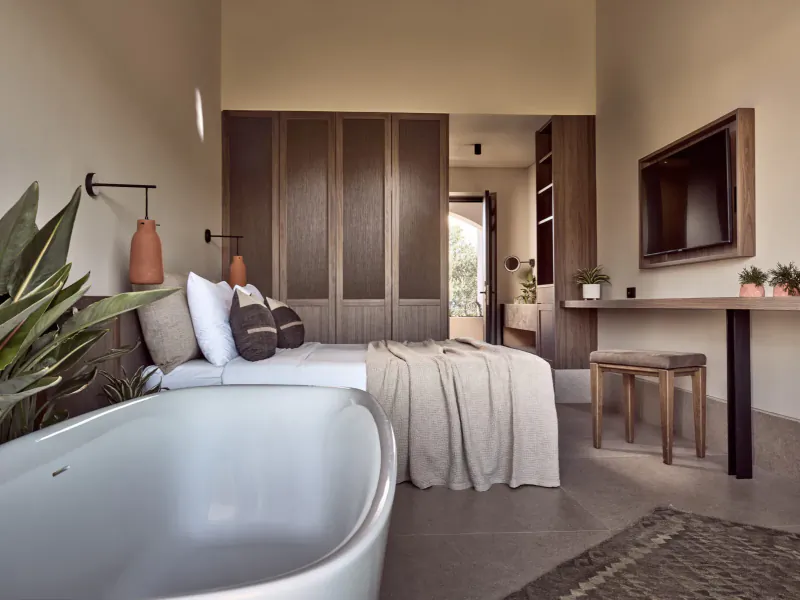 Luxurious Contessina Hotel bedroom in Zakynthos with king bed, freestanding bathtub, wooden cabinets, plants, and wall TV.