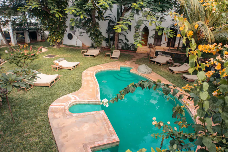 Aerial view of Kijani Hotel's serene turquoise pool surrounded by lounge chairs, lush tropical gardens, and white Swahili architecture on Lamu Island.