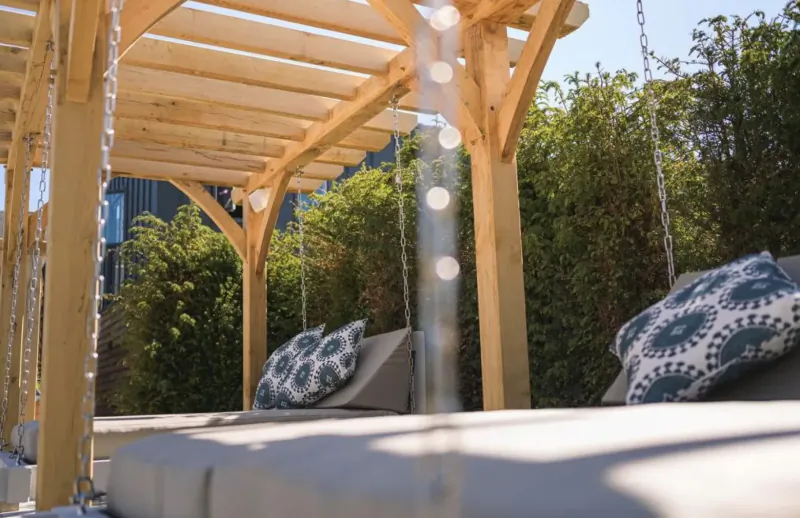 Wooden pergola with hanging chains, cushioned swing seat, and lush green hedges at a spa hotel.