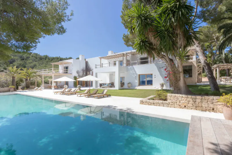 Luxurious white Ibizan villa with infinity pool, lounge chairs, palms, and sea view in Balearic Islands