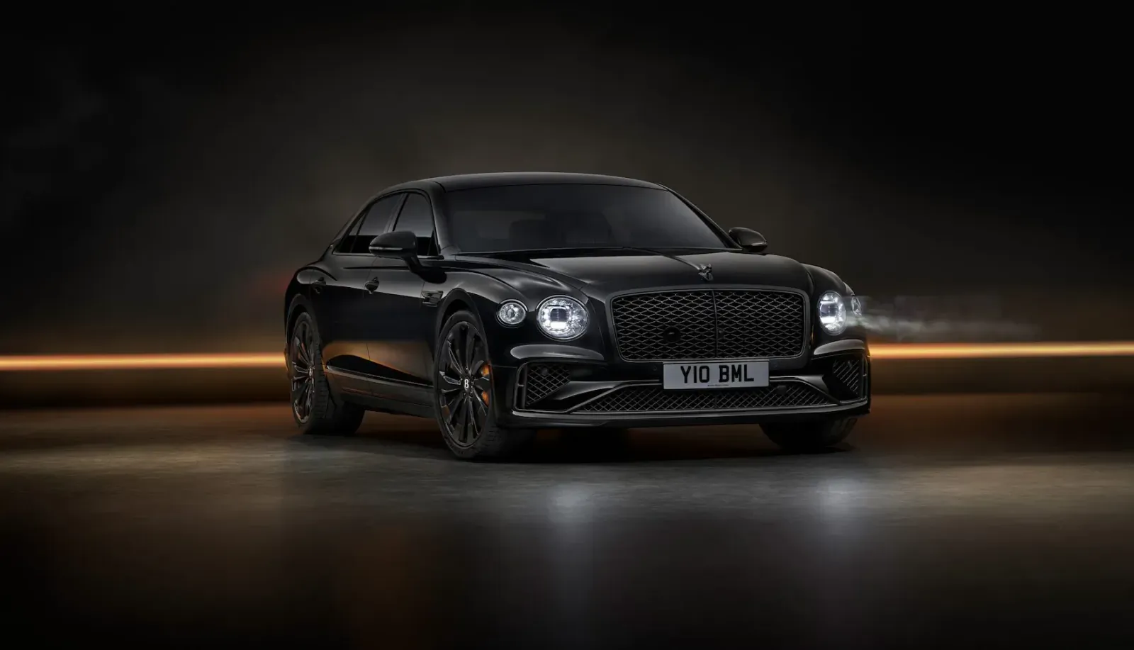 Black Bentley Flying Spur Black Edition, sleek coupe sedan with 'WNA 62L' plate, glowing headlights on dark road.