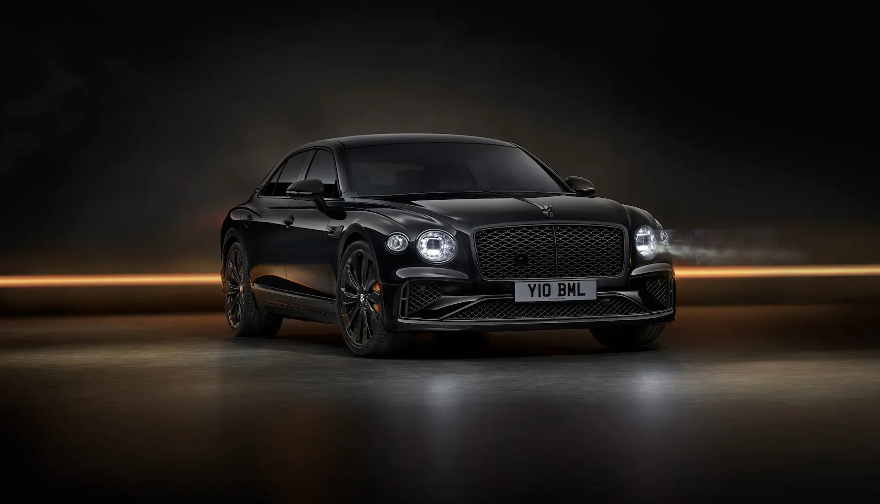 Black Bentley Flying Spur Black Edition, sleek coupe sedan with 'WNA 62L' plate, glowing headlights on dark road.