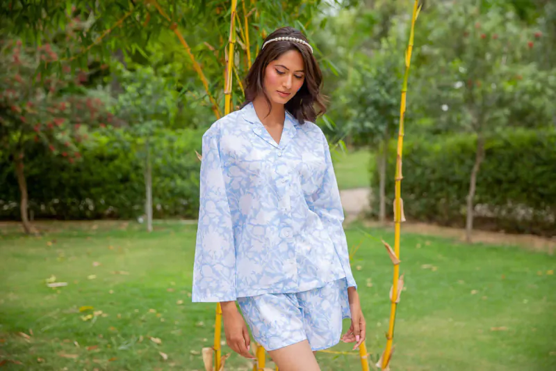 Woman in blue floral pajamas stands by swing in lush green garden
