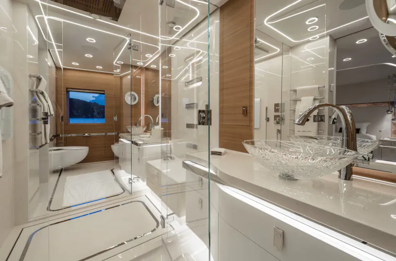 Luxurious yacht bathroom with glass shower, white toilet, double sinks, wood accents, mirrors, and TV.